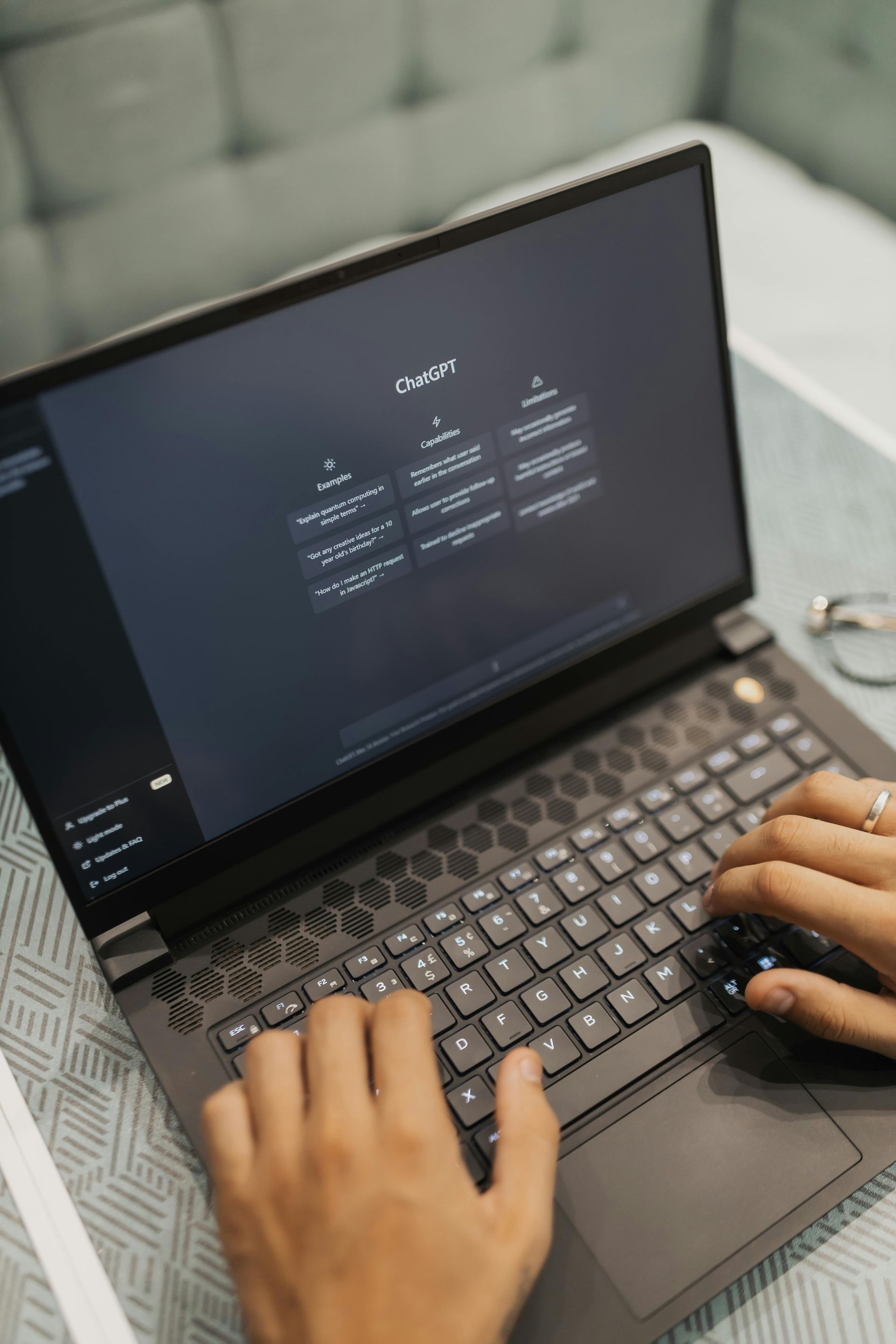 Person typing on a laptop with a dark screen displaying a user interface. Hands visible.