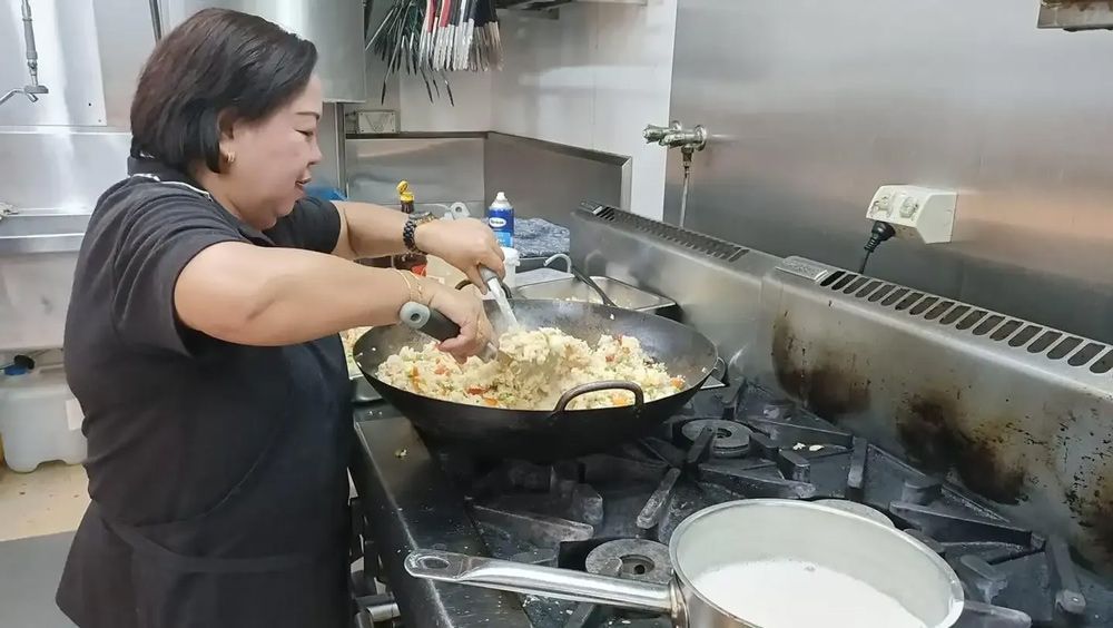 A Woman Is Cooking Food In A Wok In A Kitchen — Leichhardt Accommodation in Mornington, QLD