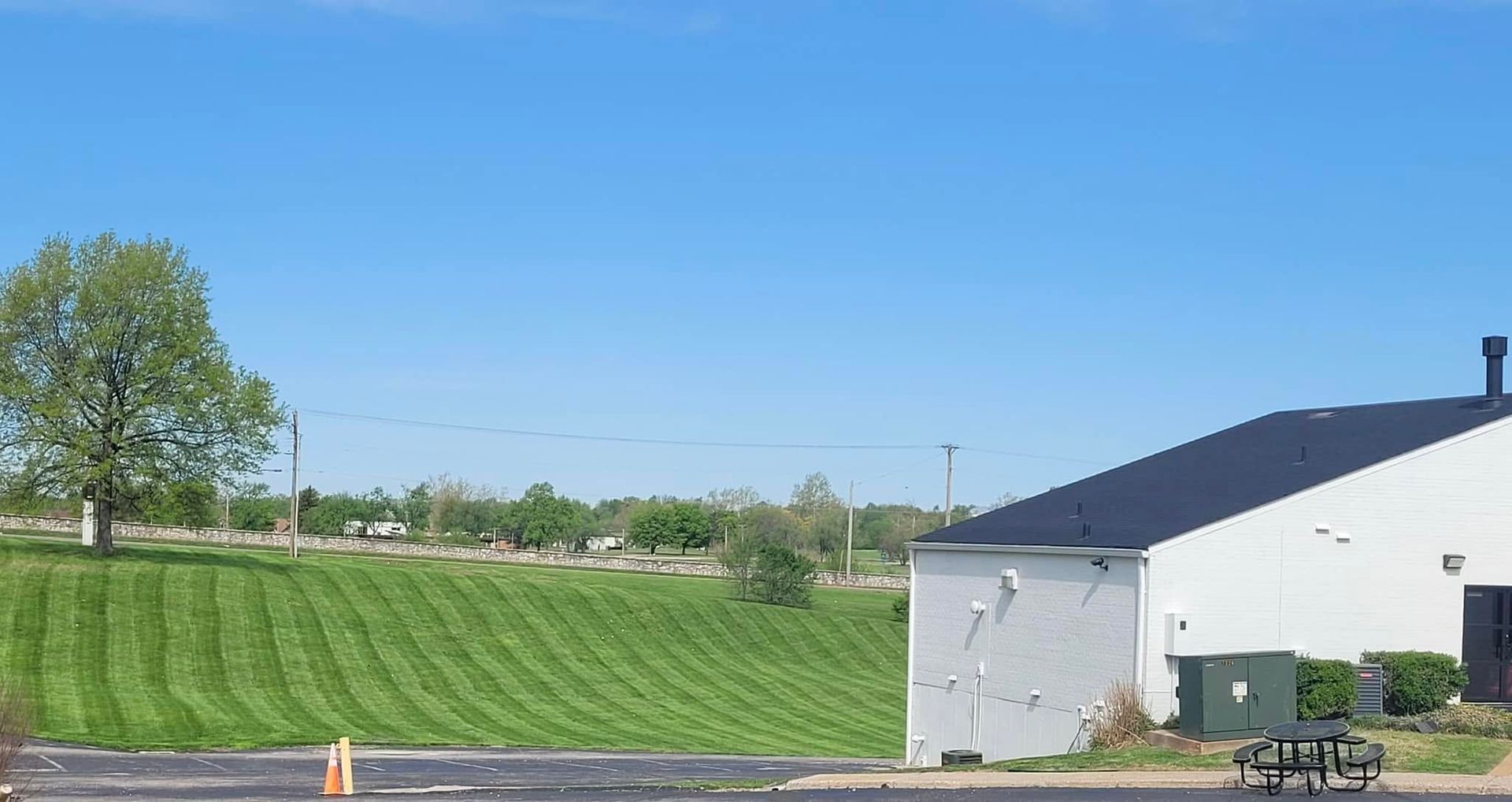 Green field beside a white building under a clear blue sky, with a tree and parked bike in the foreground