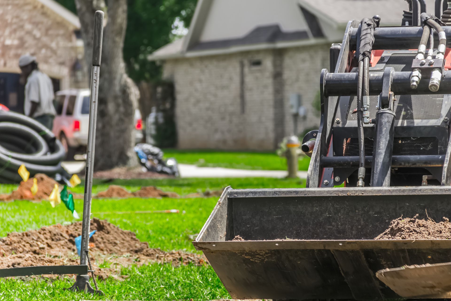 Roadwork tools and soil in a grassy yard near a stone building