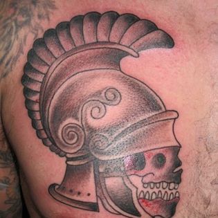 A man has a tattoo of a spartan helmet with a skull on his back.