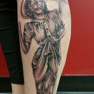 A black and white tattoo of a woman holding an umbrella on a leg.