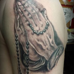 A black and white tattoo of praying hands with a rosary.