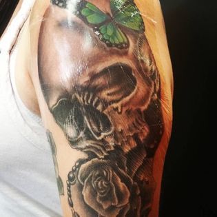 A woman has a tattoo of a skull and roses on her arm.