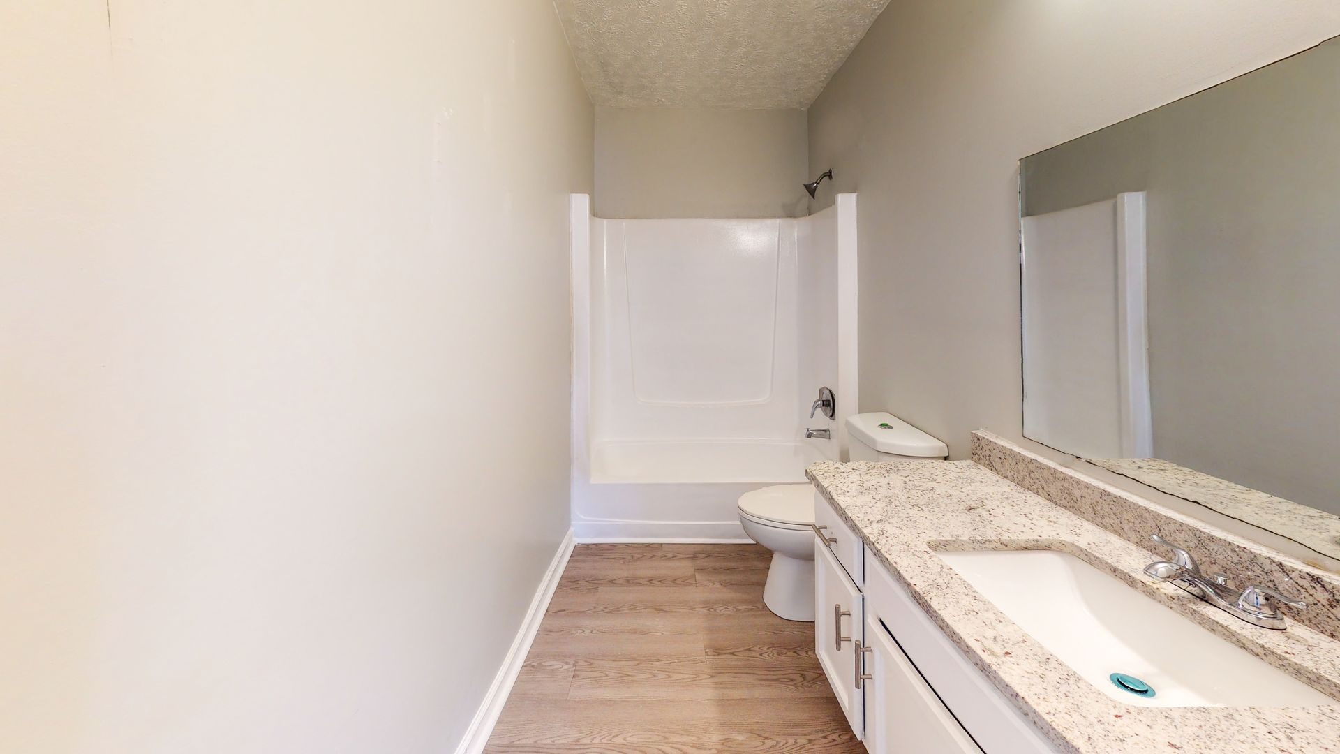 Small bathroom with white walls, toilet, shower curtain, and beige vanity countertop with mirror