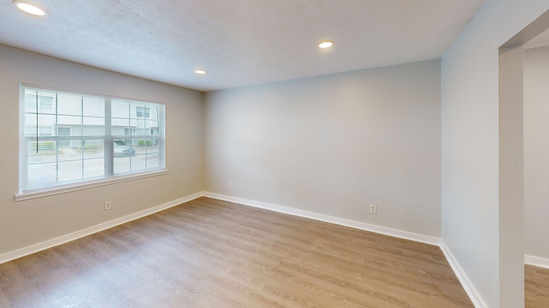 Empty white living room with wood floors, recessed lights, and a staircase on the left