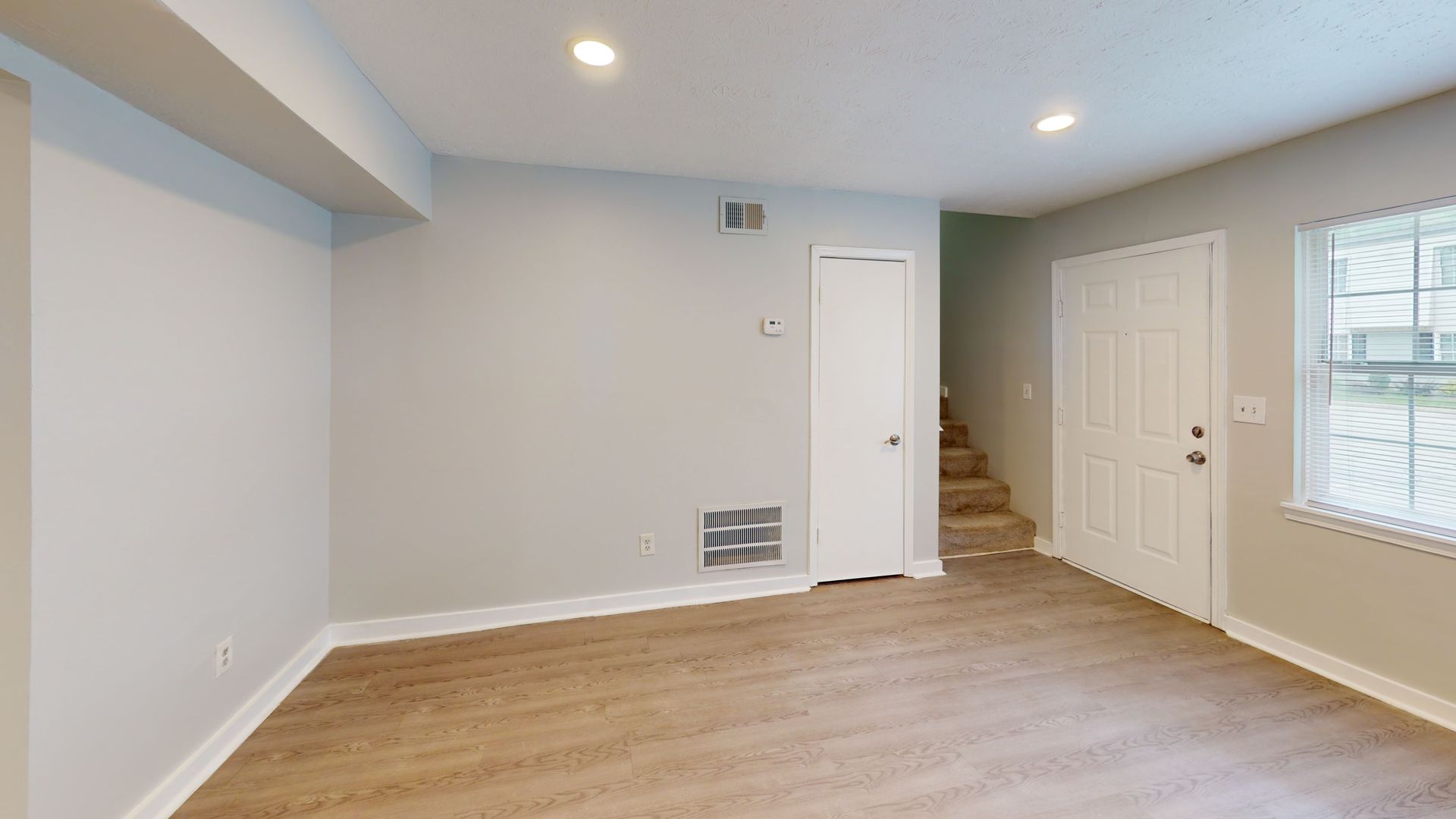 Empty modern room with light wood floors, white walls, recessed lighting, and a small staircase at the back right