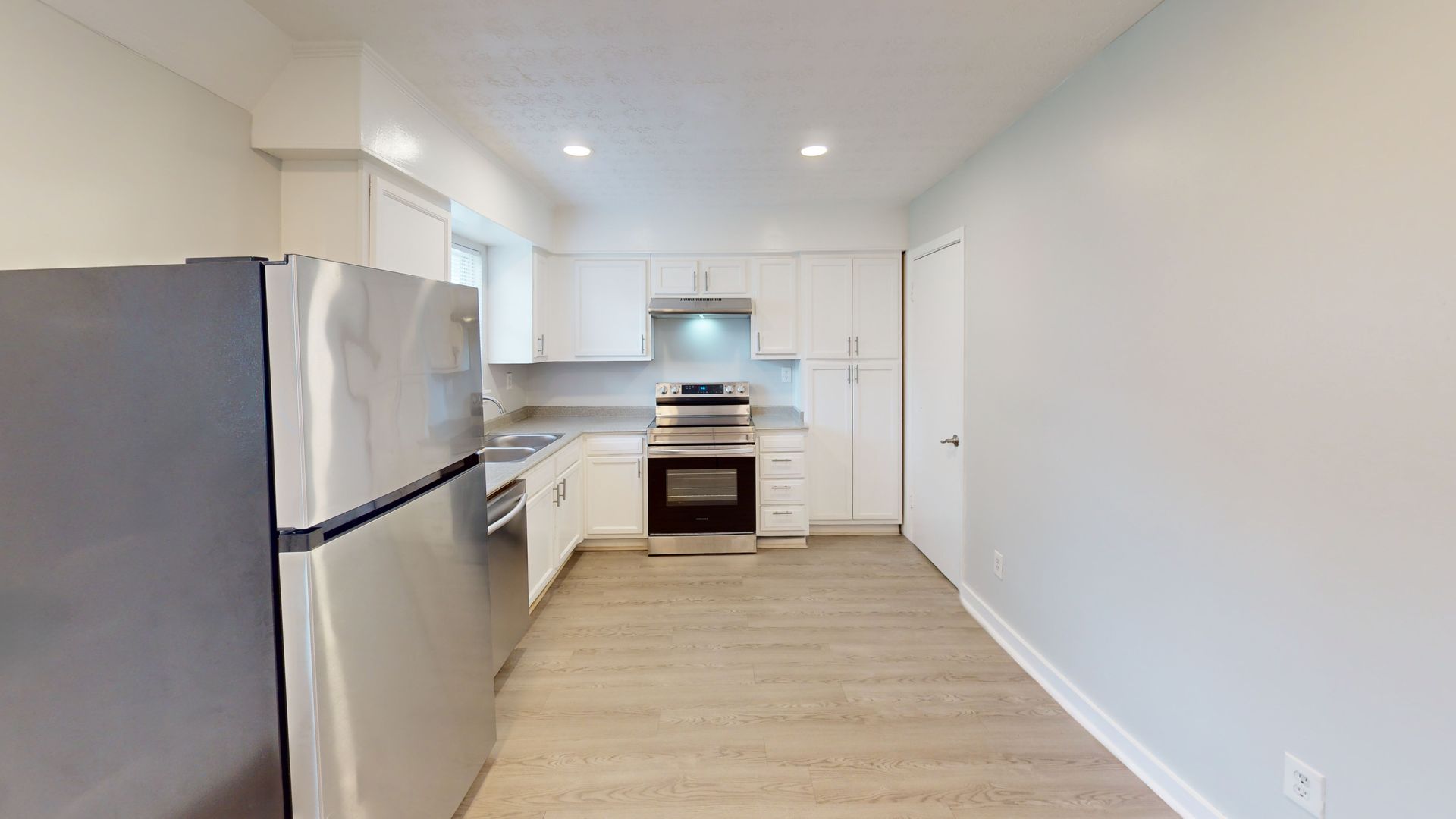 Bright modern kitchen with stainless steel appliances, white cabinets, and light wood flooring.