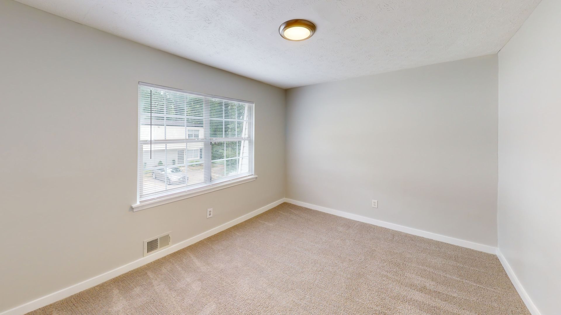 Empty beige bedroom with carpet, window, and ceiling light