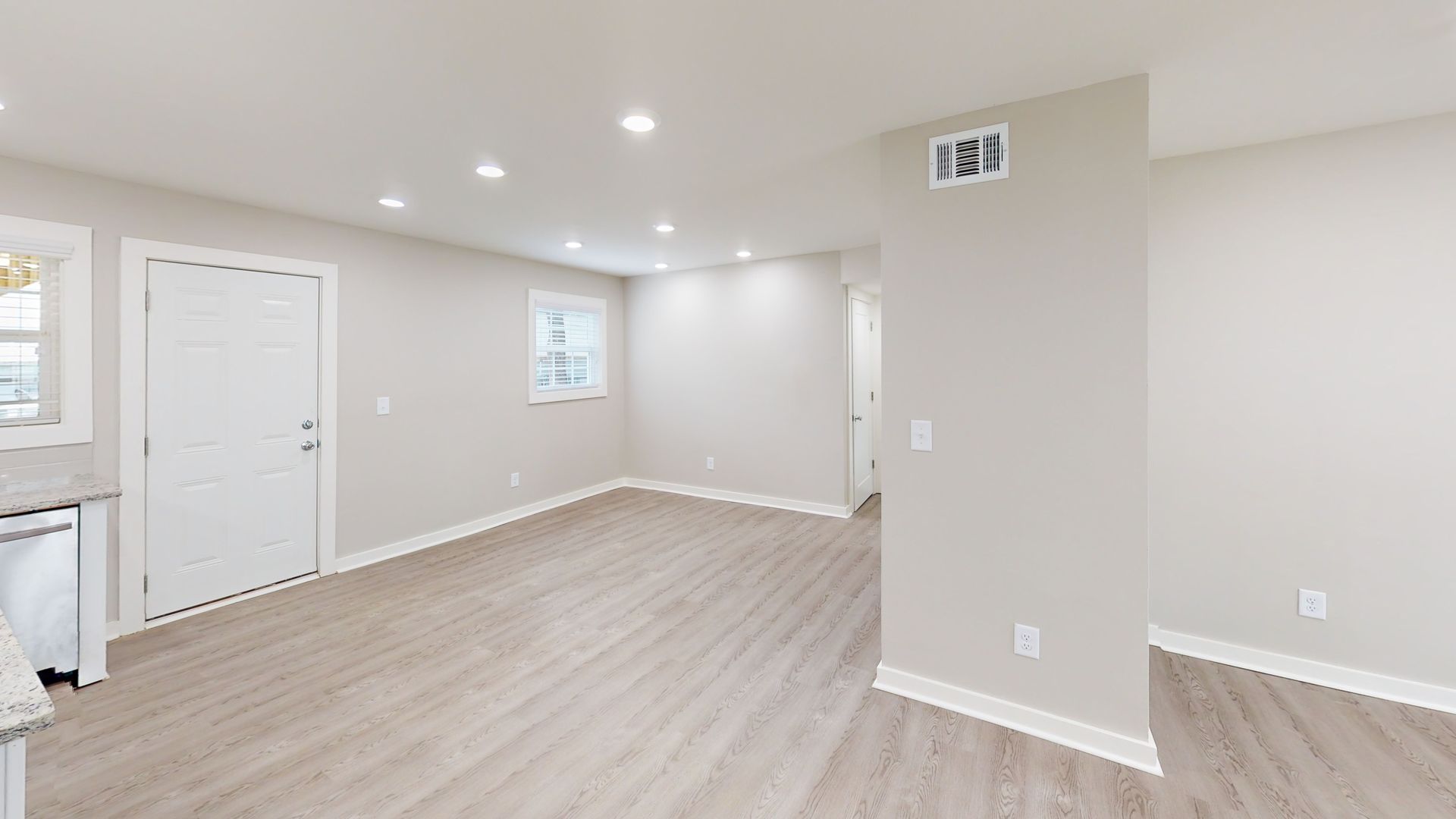 Empty bright room with light wood floors, white walls, recessed lights, and a small window.