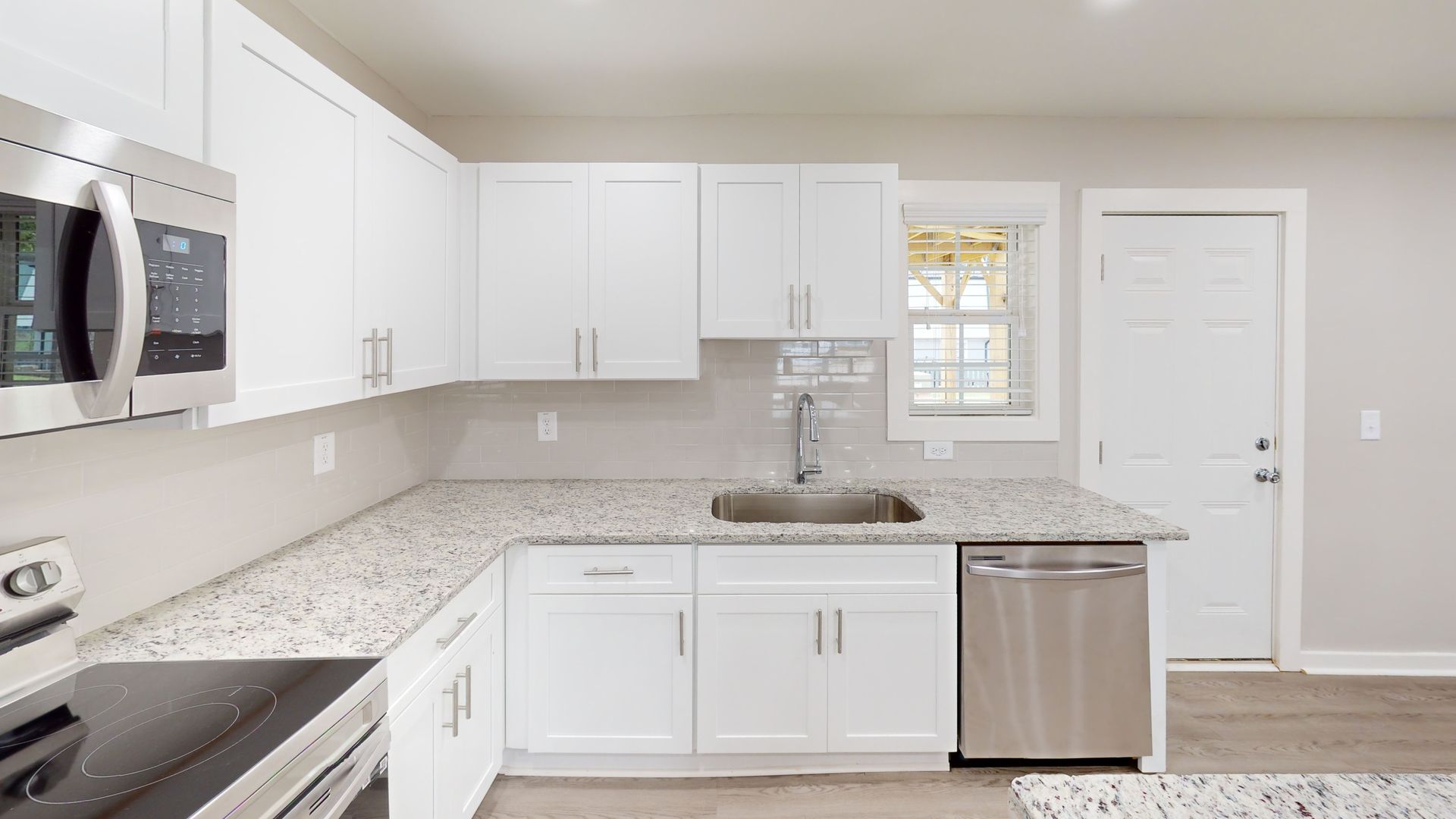 Bright modern kitchen with white cabinets, gray backsplash, stainless steel appliances, and a window by the sink