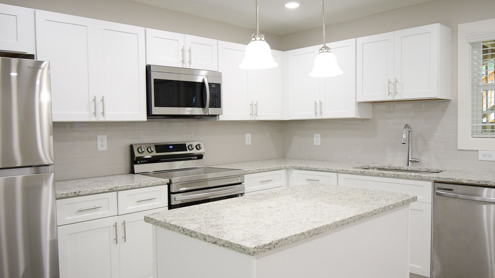 Bright white modern kitchen with stainless steel appliances and a granite island countertop