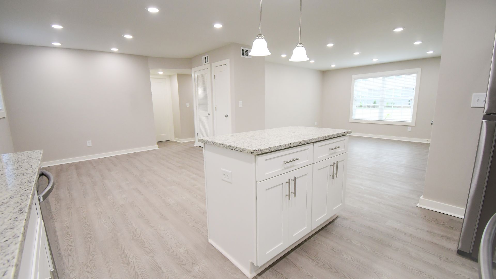 Bright modern open-concept kitchen and living area with white cabinets, gray floors, and recessed lighting