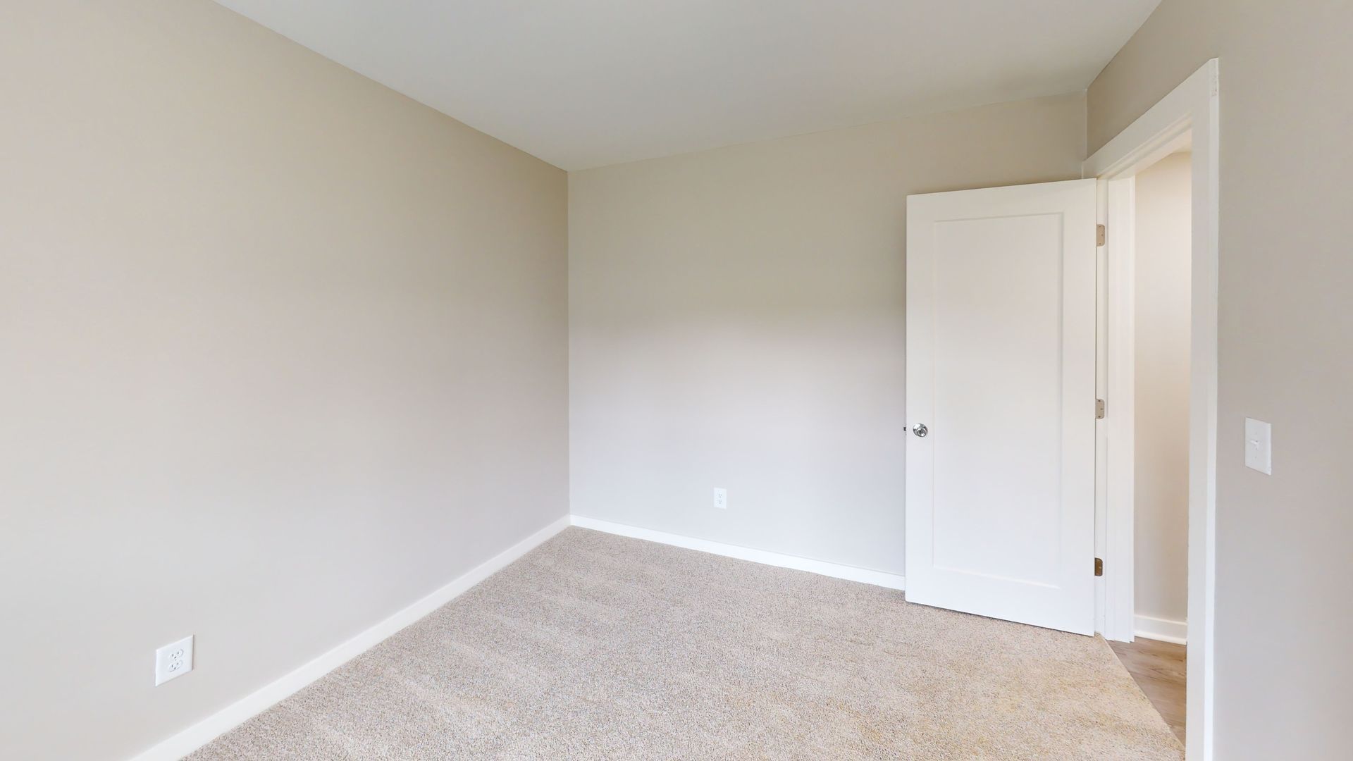 Empty beige bedroom with carpet, white door, and light gray walls
