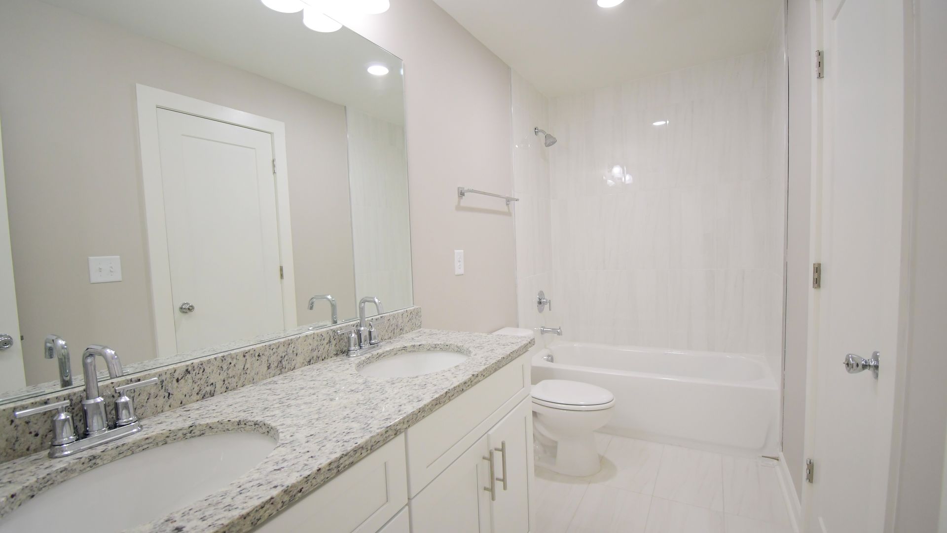 Bright white bathroom with double vanity, granite countertop, large mirror, and bathtub/shower combo.