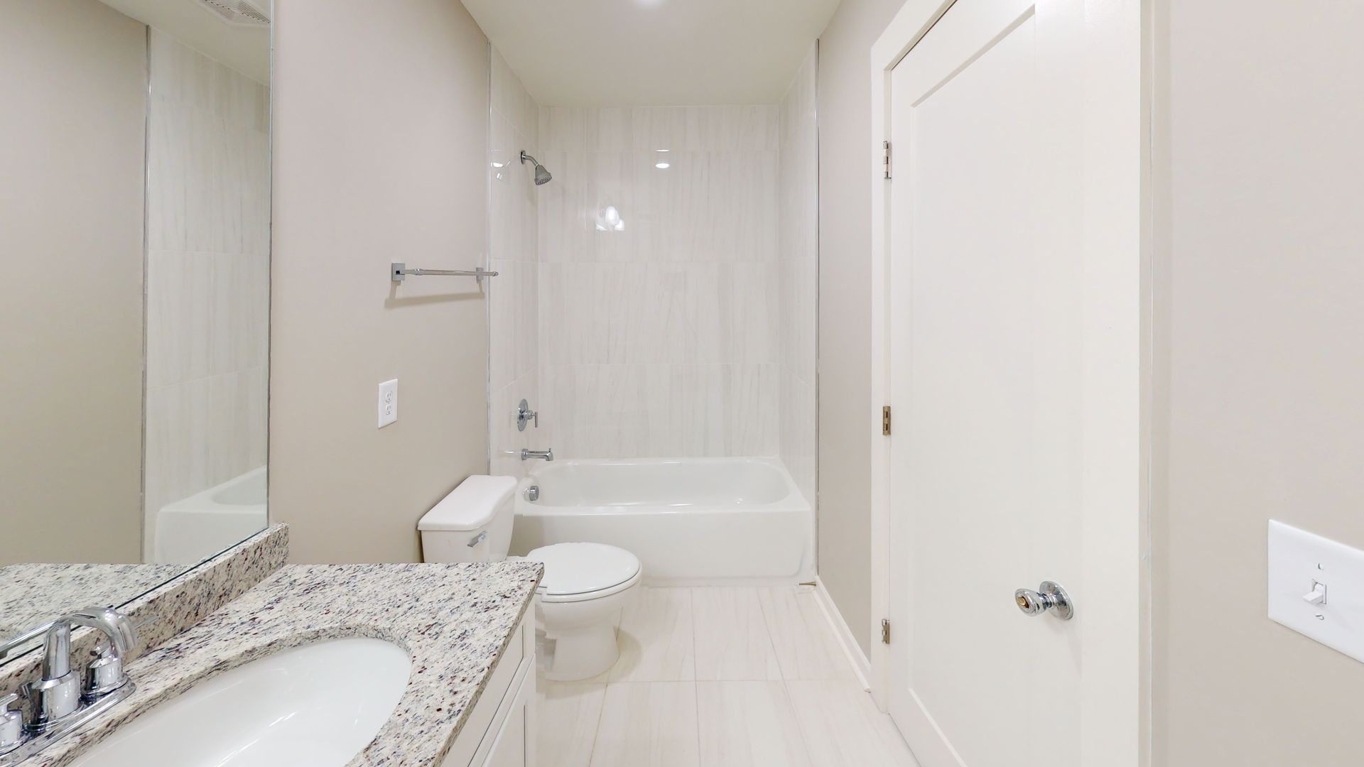 Bright modern bathroom with double sink, large mirror, and a tub shower in the background