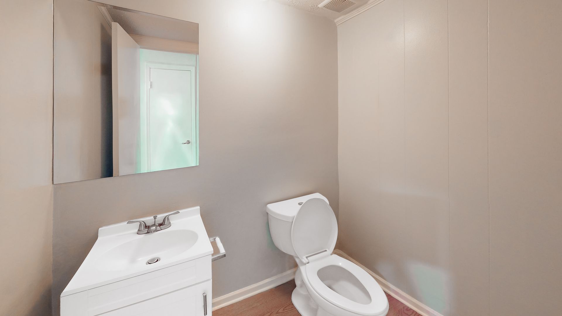 Small beige bathroom with a white sink, mirror cabinet, and toilet.