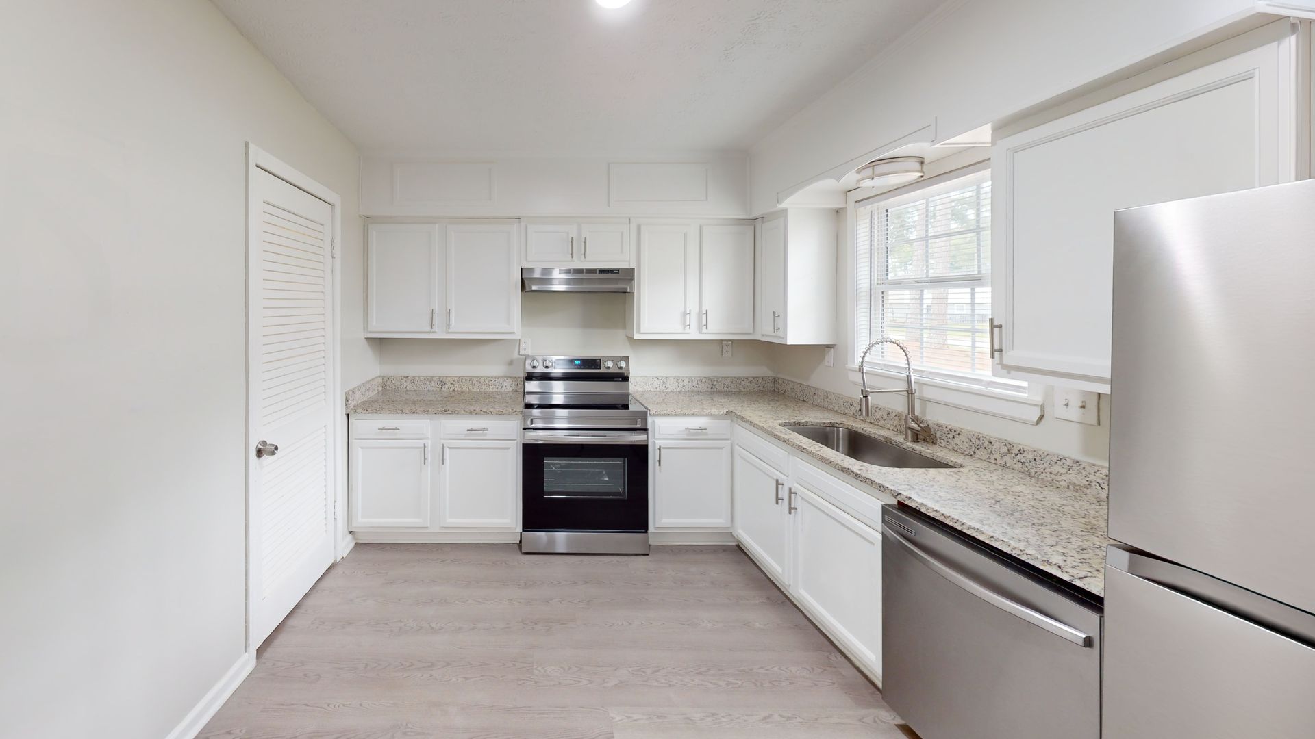 Bright white modern kitchen with stainless steel appliances, granite counters, and a large window.