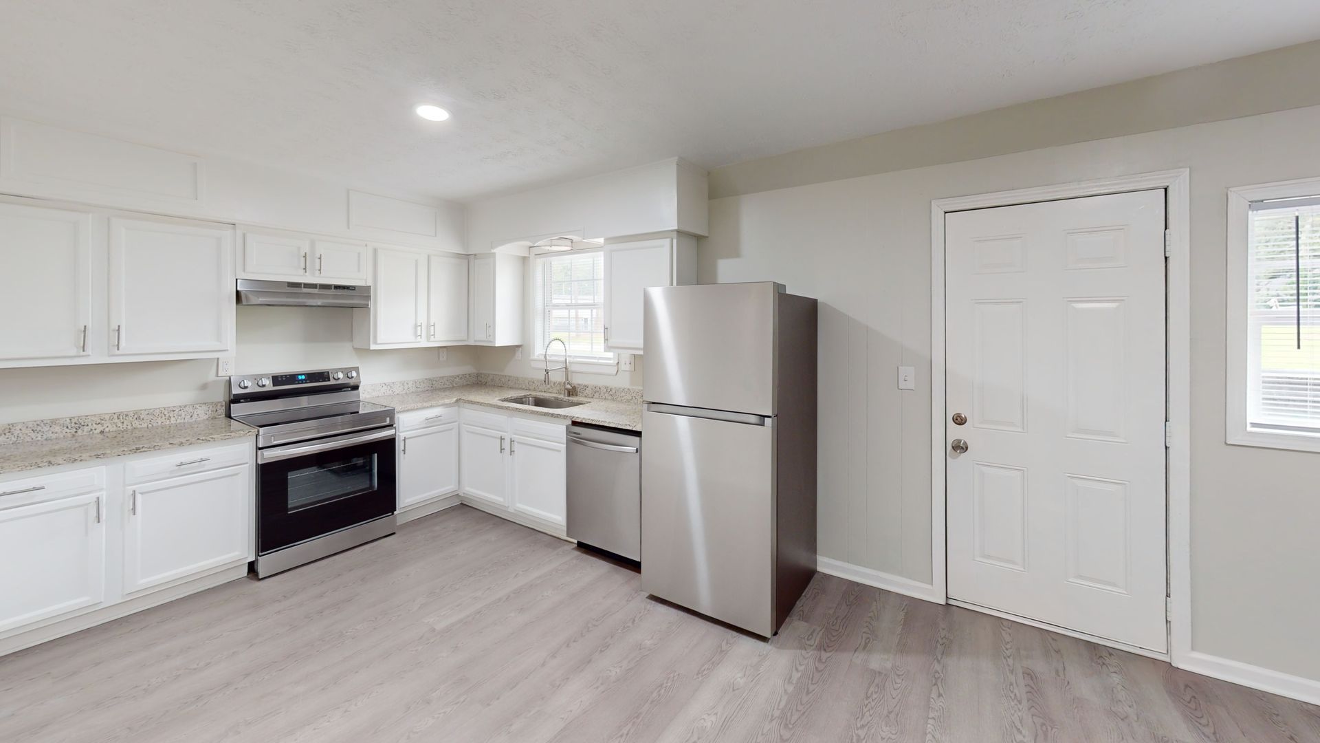 Bright empty kitchen with white cabinets, stainless steel fridge, black stove, and light wood floors