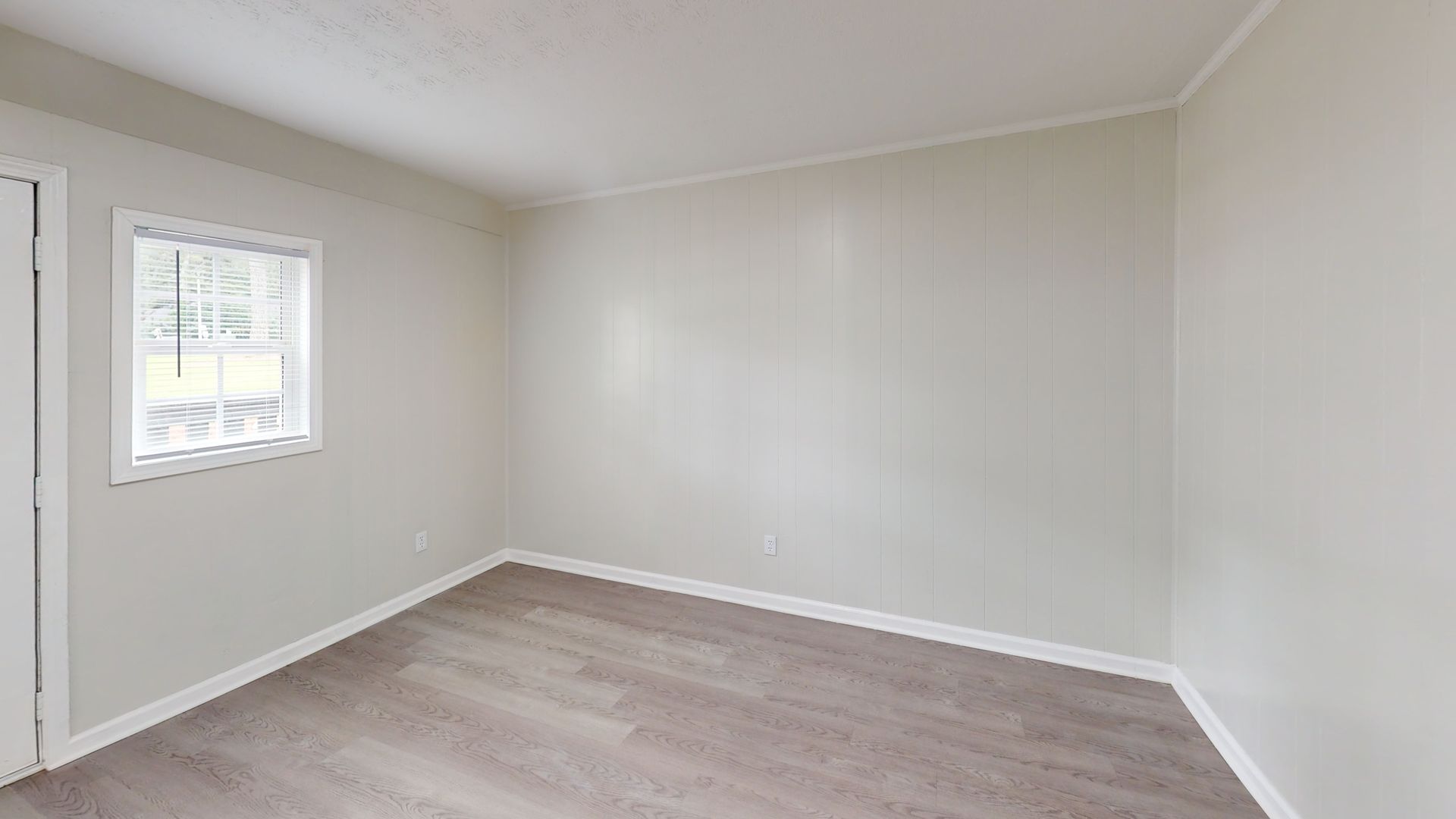 Empty beige room with gray walls, light wood floor, and a small window.