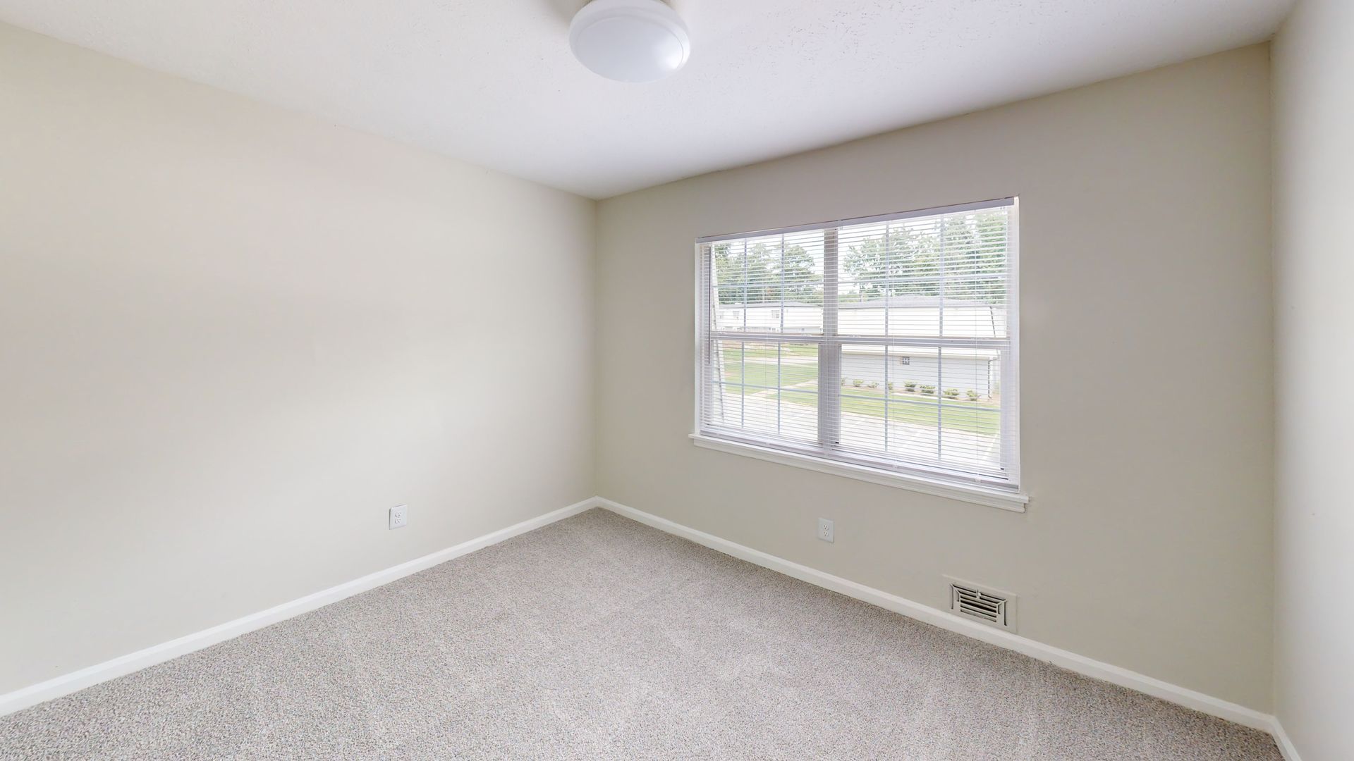 Empty light-gray bedroom with carpeted floor and a window overlooking a street
