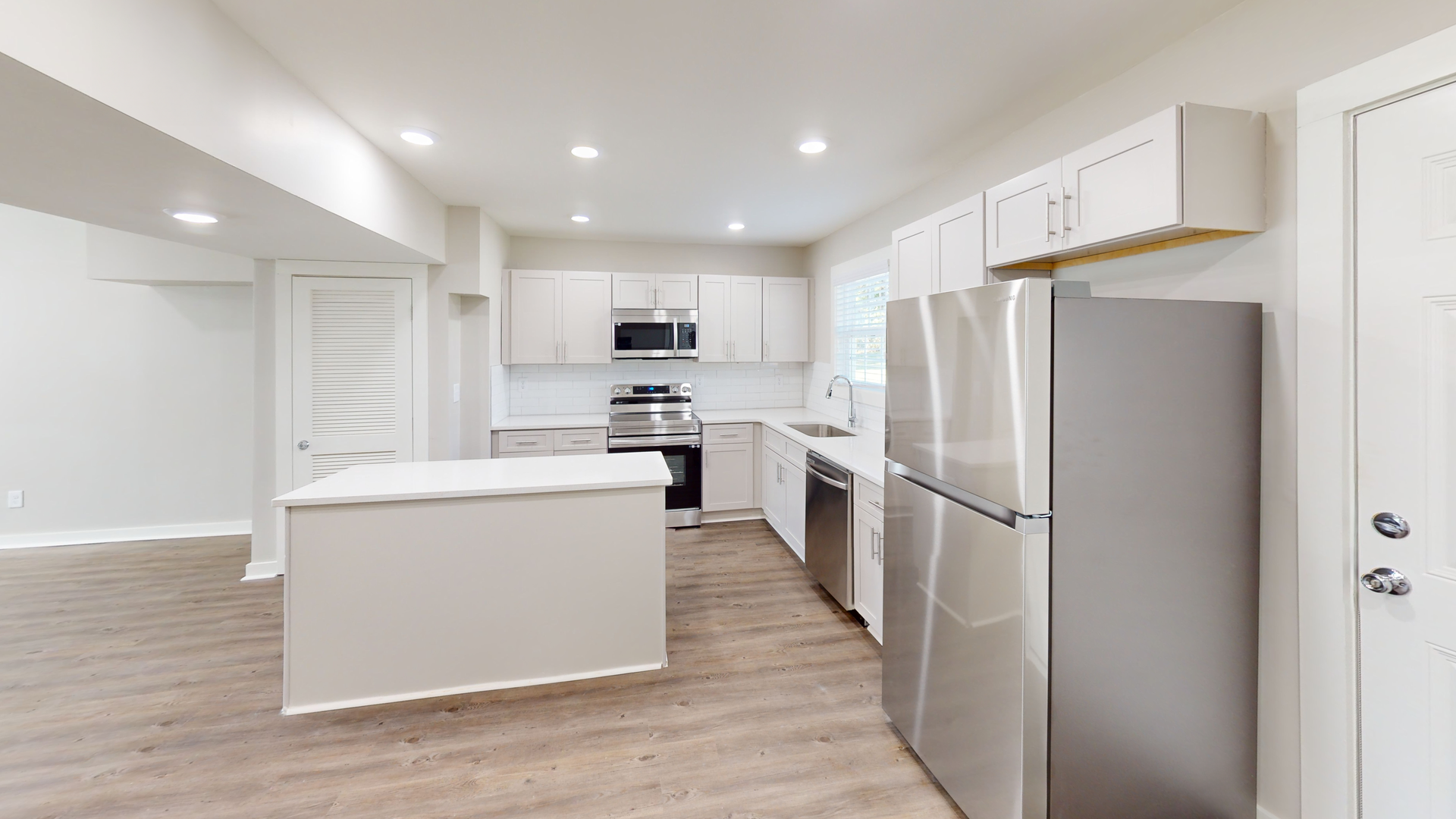 Bright modern kitchen with white cabinets, stainless steel appliances, and light wood floors