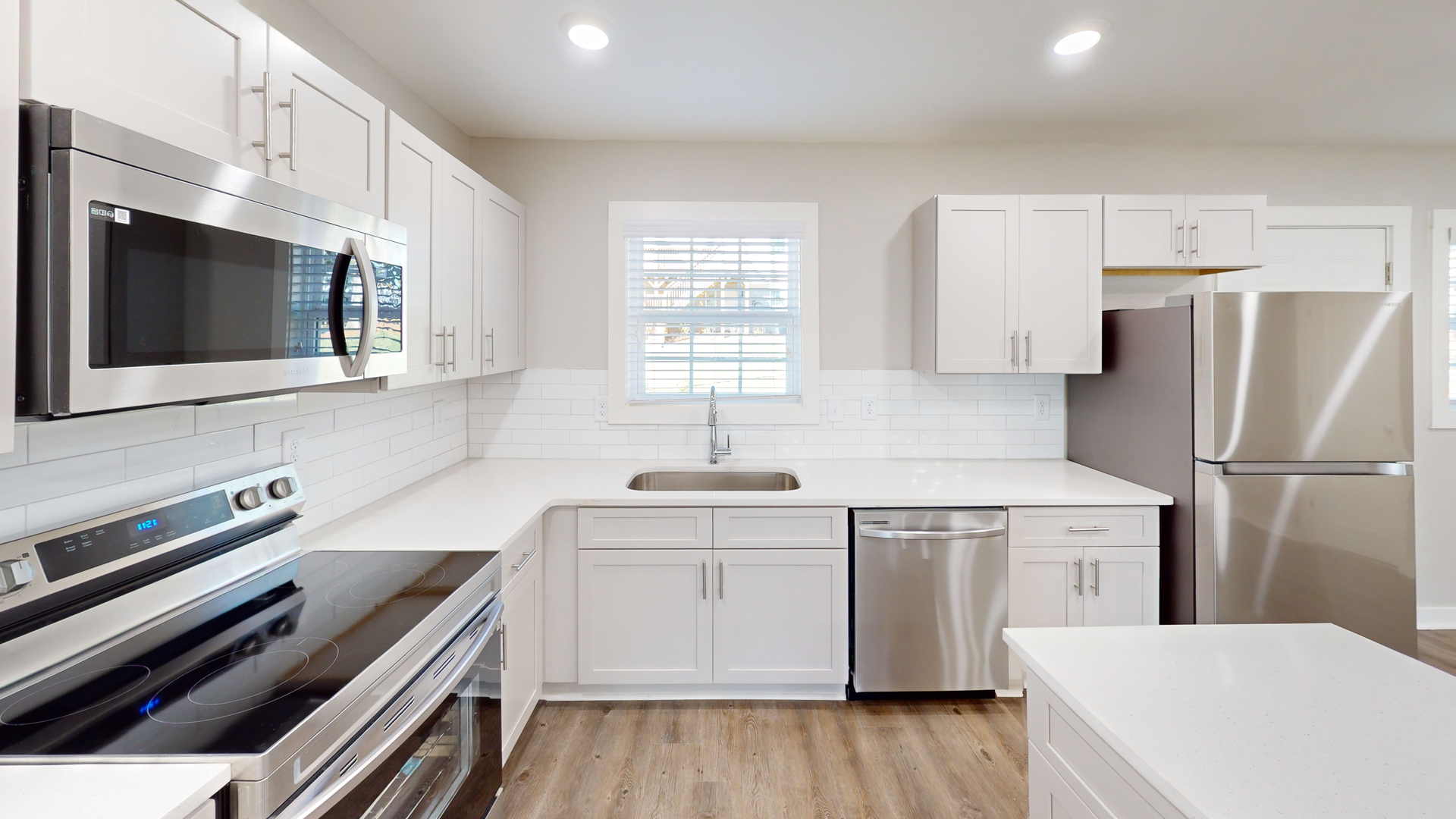 Bright modern white kitchen with stainless steel appliances and wood flooring