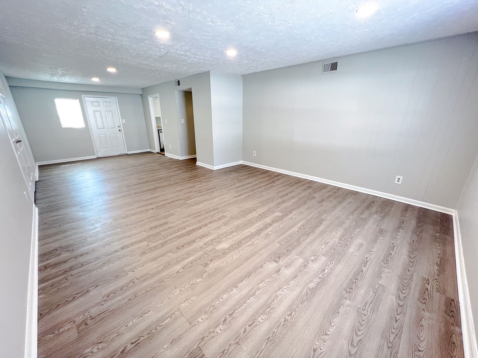 Empty unfurnished living room with light wood flooring, white walls, and recessed ceiling lights.