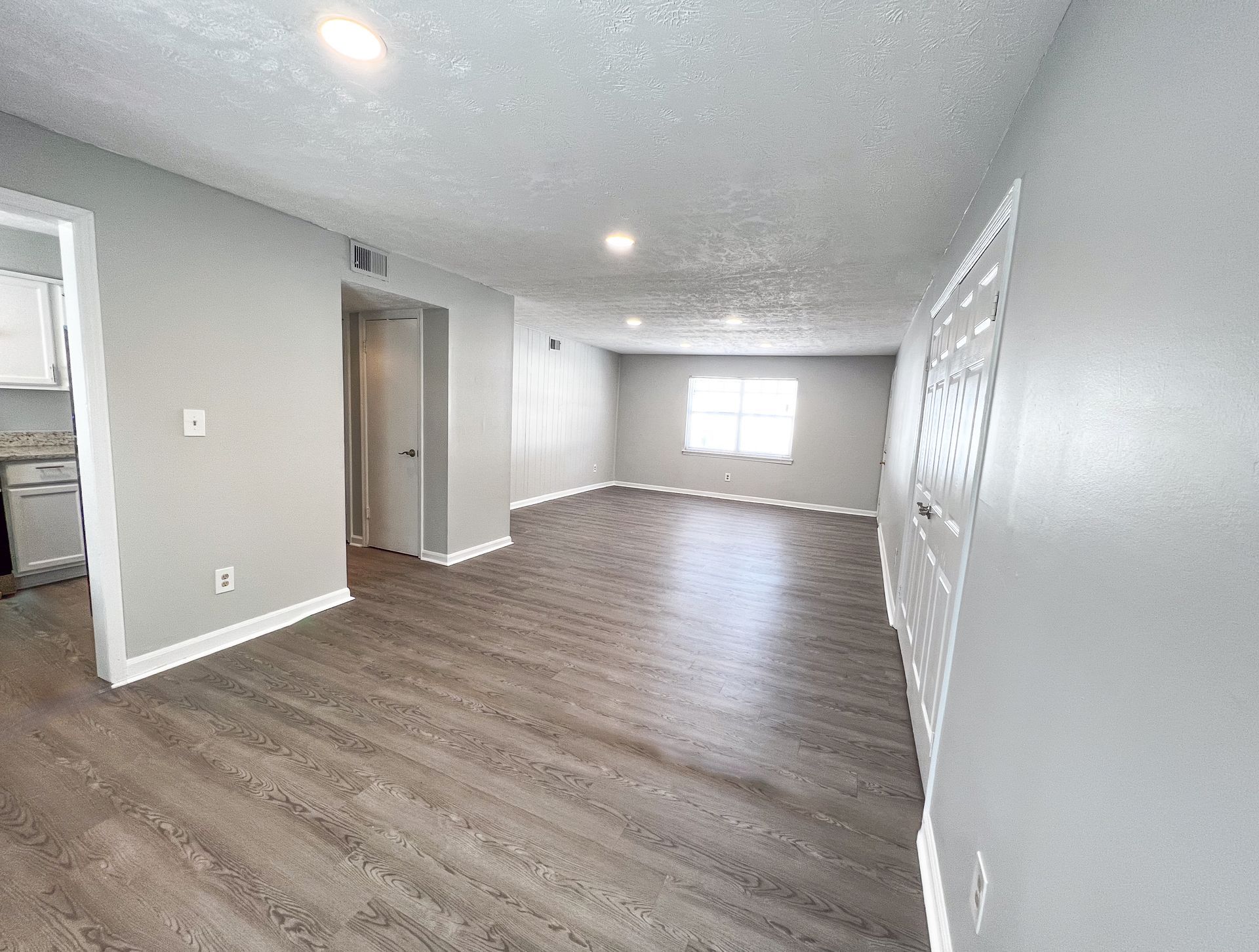 Empty modern living room with gray walls, wood-look flooring, and bright windows.