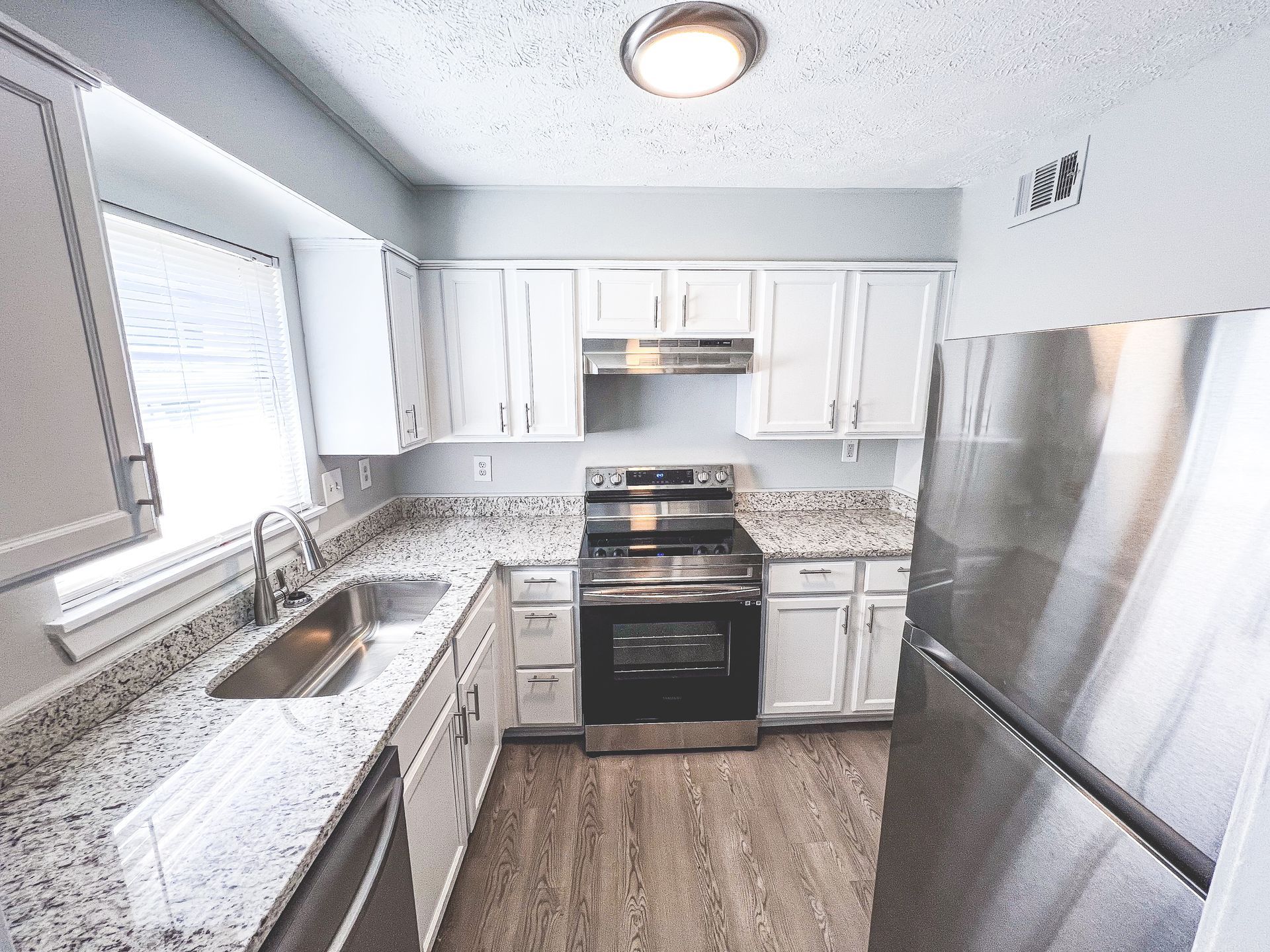 Bright modern kitchen with white cabinets, stainless steel appliances, granite counters, and wood floors