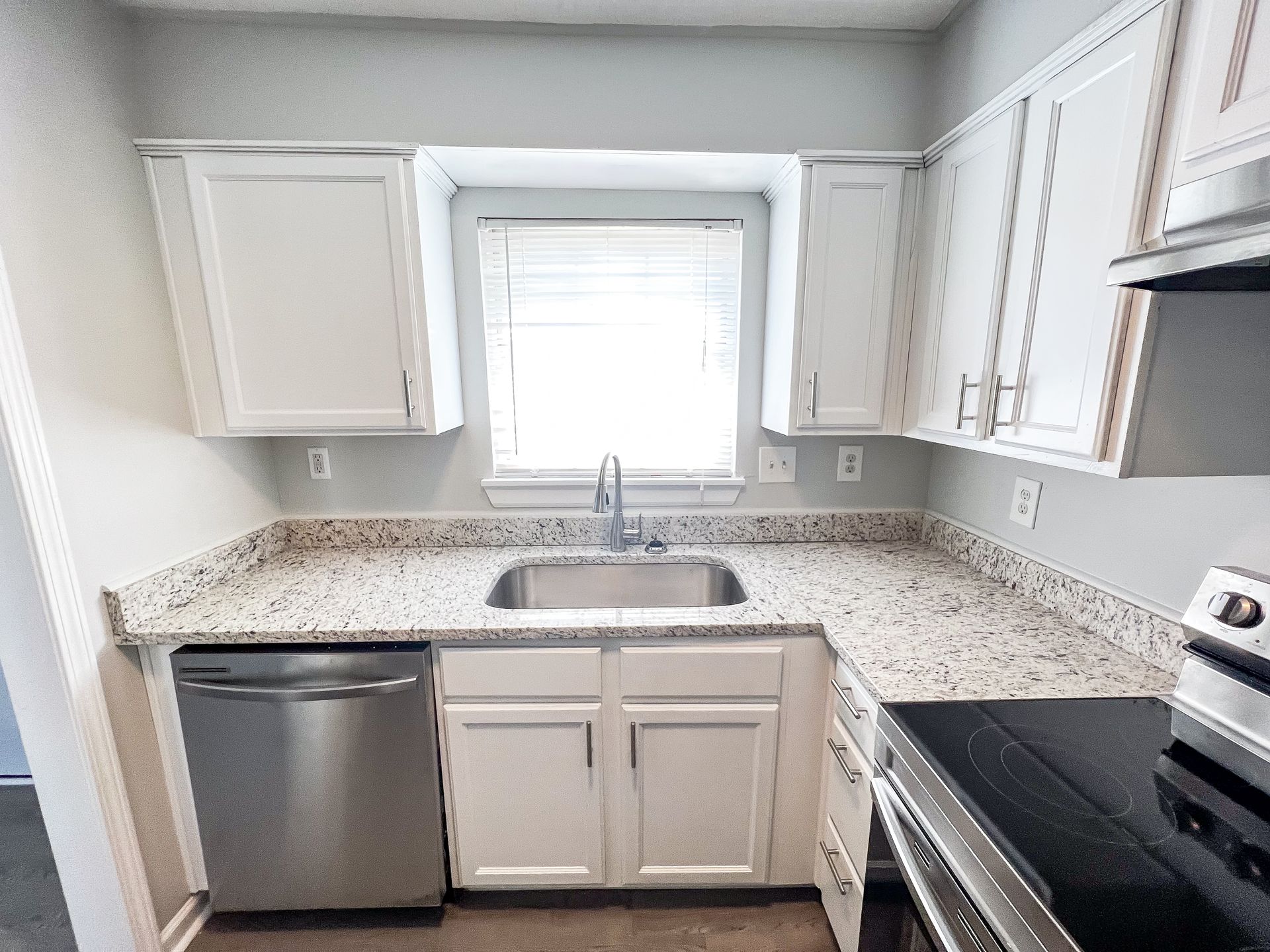 Bright kitchen with white cabinets, granite countertops, stainless sink and dishwasher, and a window over the sink