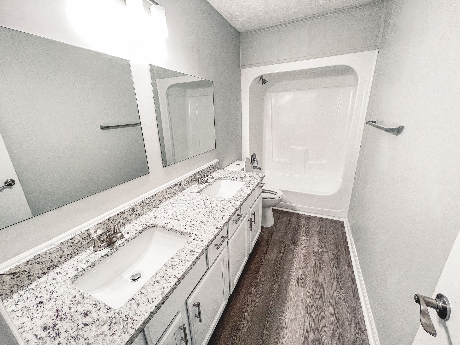 Modern bathroom with long vanity, granite countertop, large mirror, and shower/tub alcove.