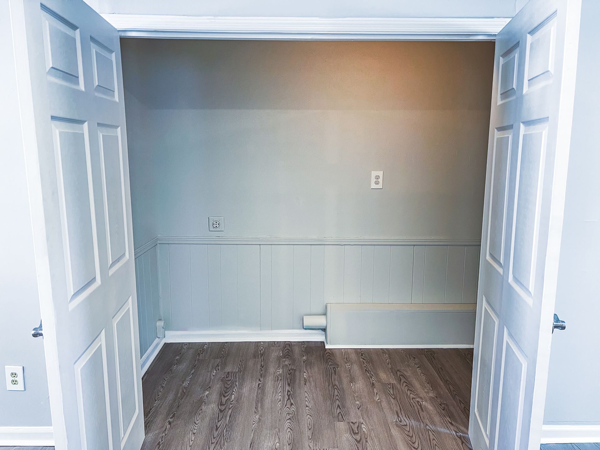 Empty room with open double doors, gray walls, white trim, and dark wood flooring