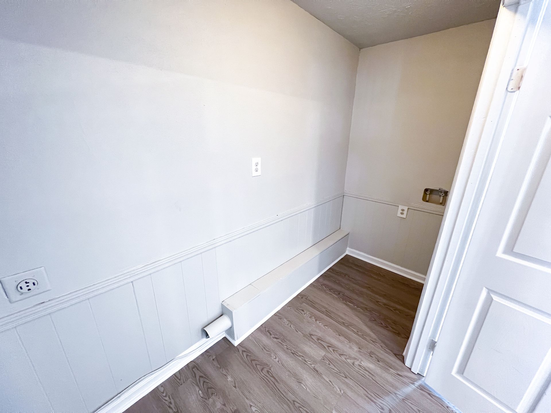 Empty small room with white walls, wainscoting, wood floor, and open door.