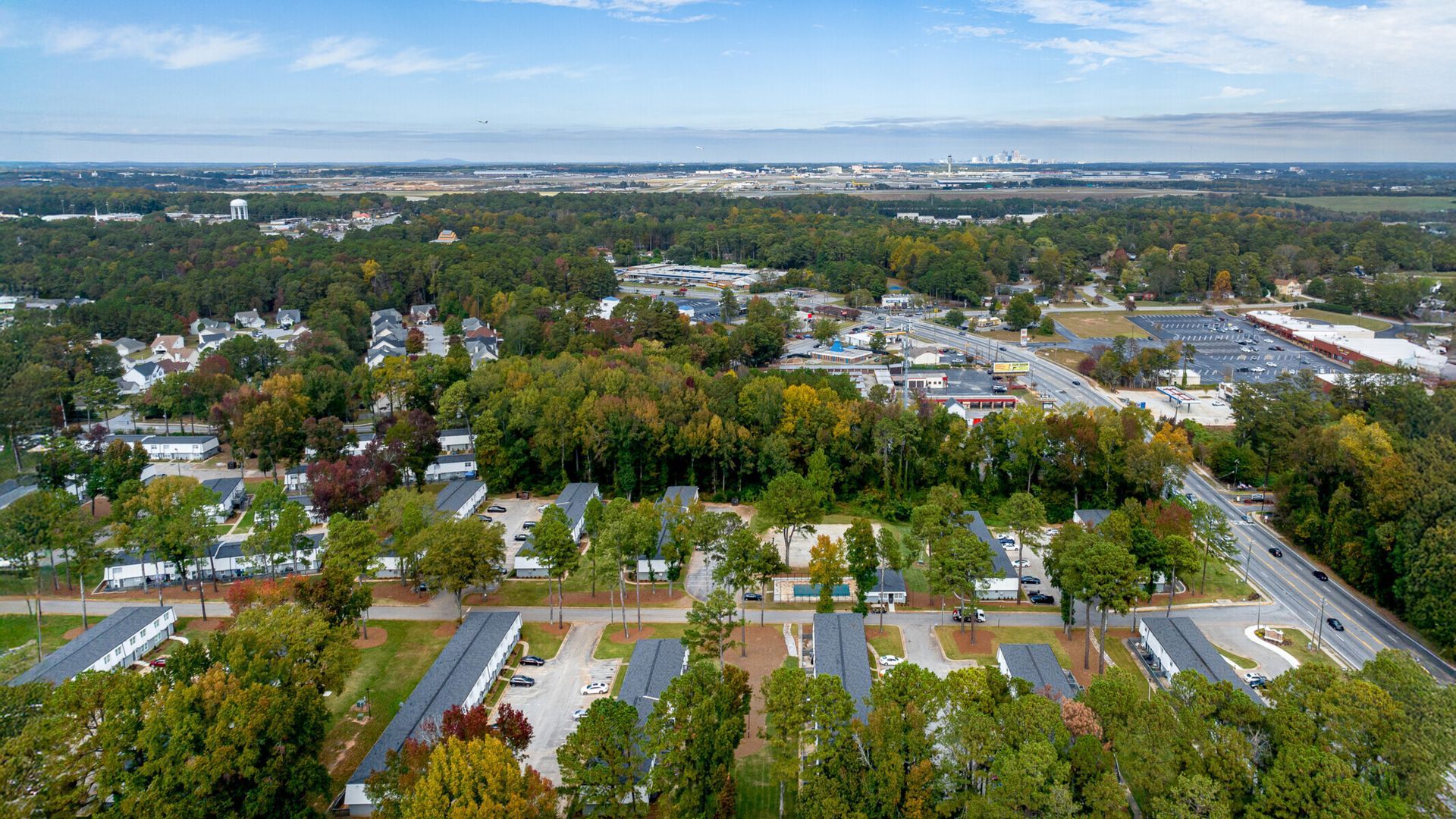 Aerial view of a suburban neighborhood with tree-lined streets, houses, and a distant skyline under a clear sky