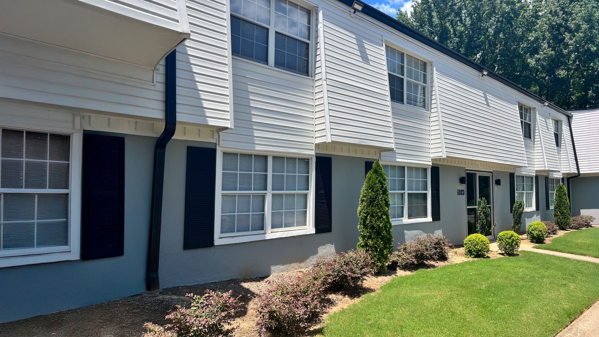Row of gray townhouses with white trim, windows, shrubs, and a sunny green lawn