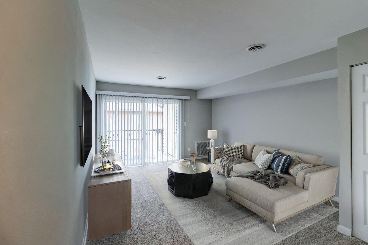 Bright, modern living room with beige sofa, TV on wooden stand, chair, plants, and light walls