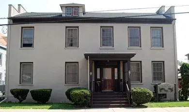 Front view of a gray two-story house with a covered entrance and steps leading up to the door