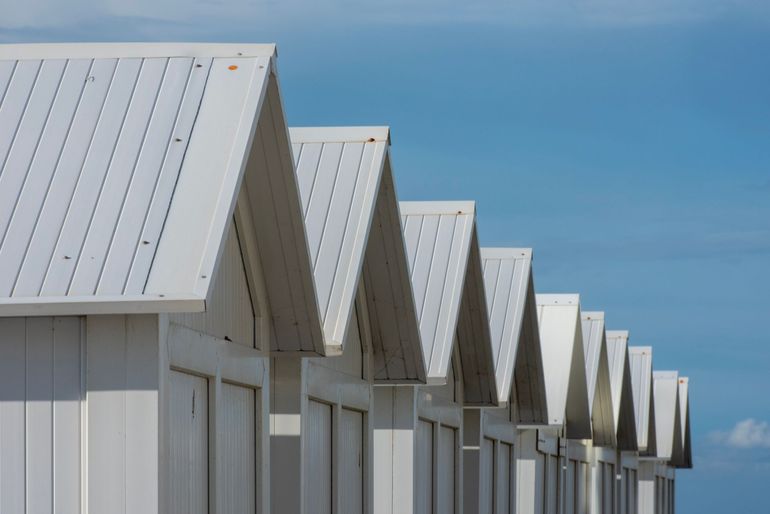 Row of white beach huts with peaked roofs against a blue sky