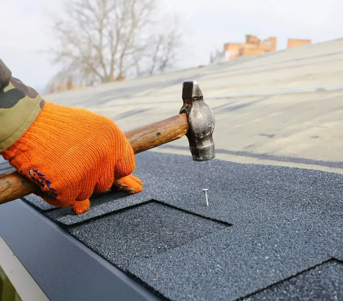 Gloved hand hammering shingles on a roof during repair work
