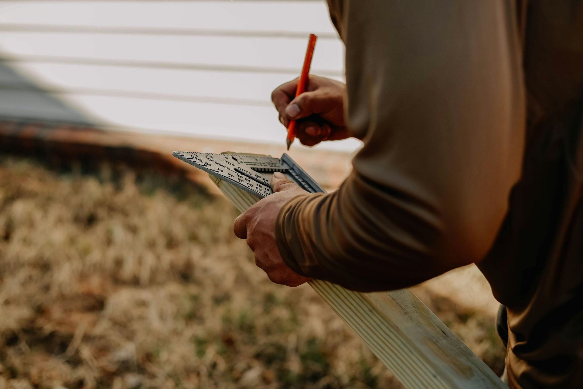 Hands sketching on a clipboard with a pencil outdoors, beside a white building and grassy field
