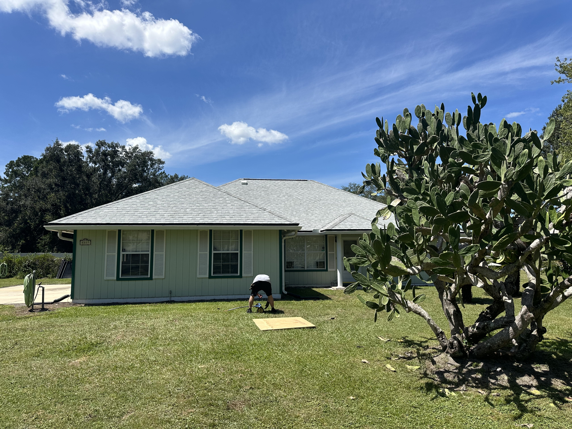 Single-story house with a white roof, green lawn, and cactus under a blue sky with clouds
