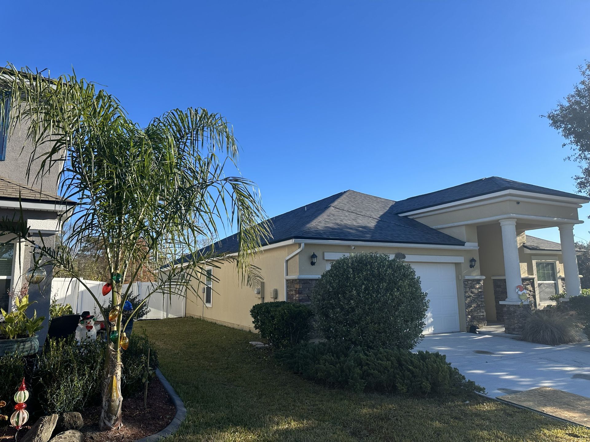 Suburban house with a blue roof, white garage, driveway, and landscaped front yard under a clear sky
