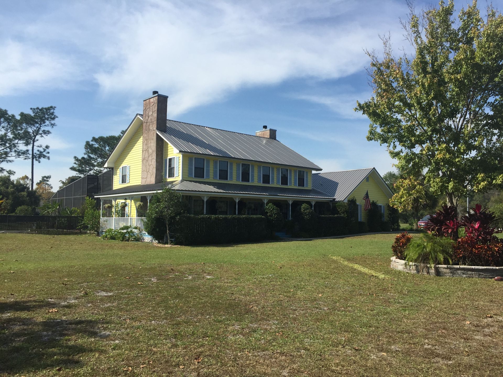 Yellow house with a dark roof beside a grassy yard under a blue sky