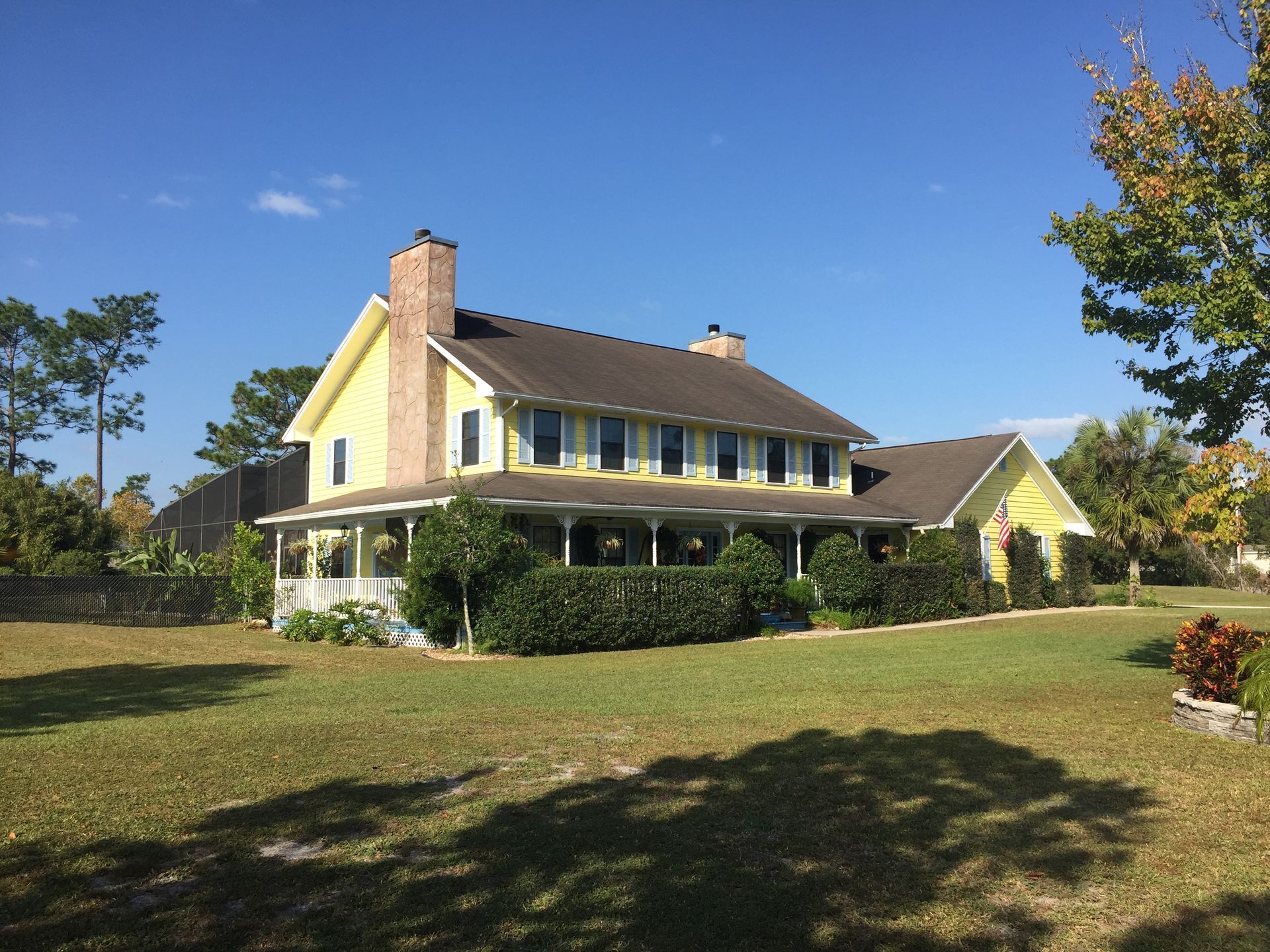 Yellow house with wraparound porch on a grassy lawn under a blue sky