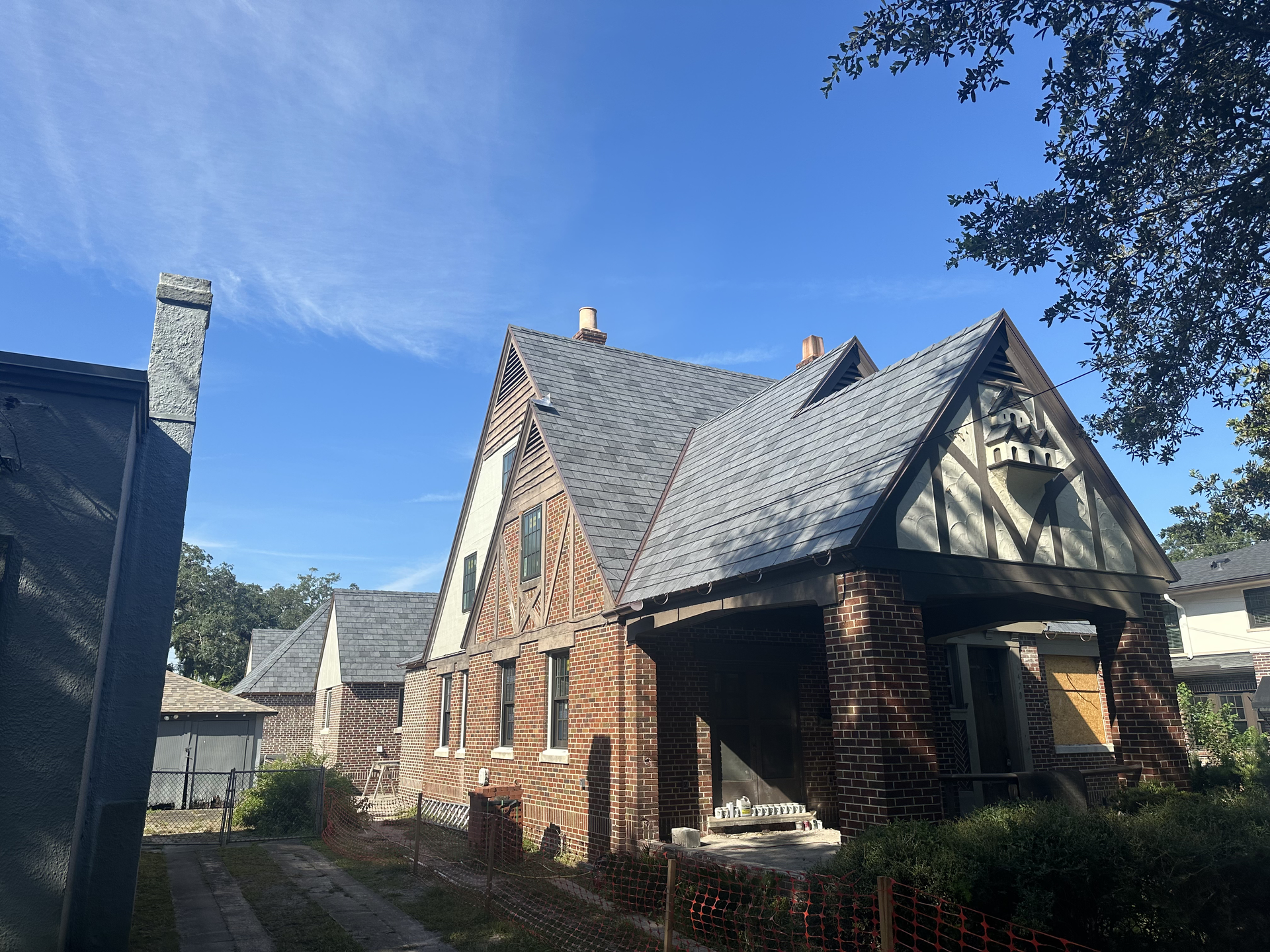 Stone cottage with steep slate roof under a bright blue sky, framed by trees and shrubs