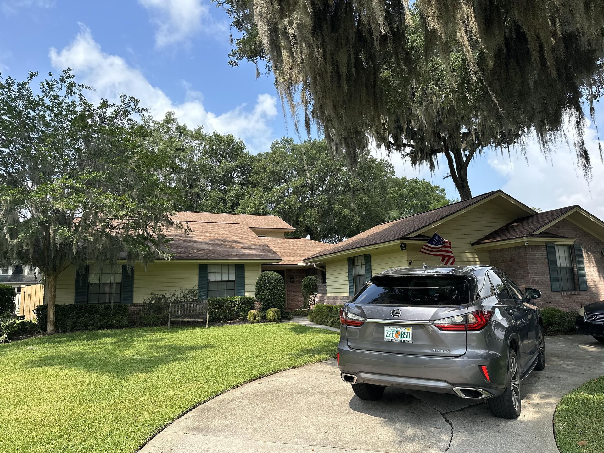 Suburban single-story house with a gray SUV parked in the driveway under a large tree