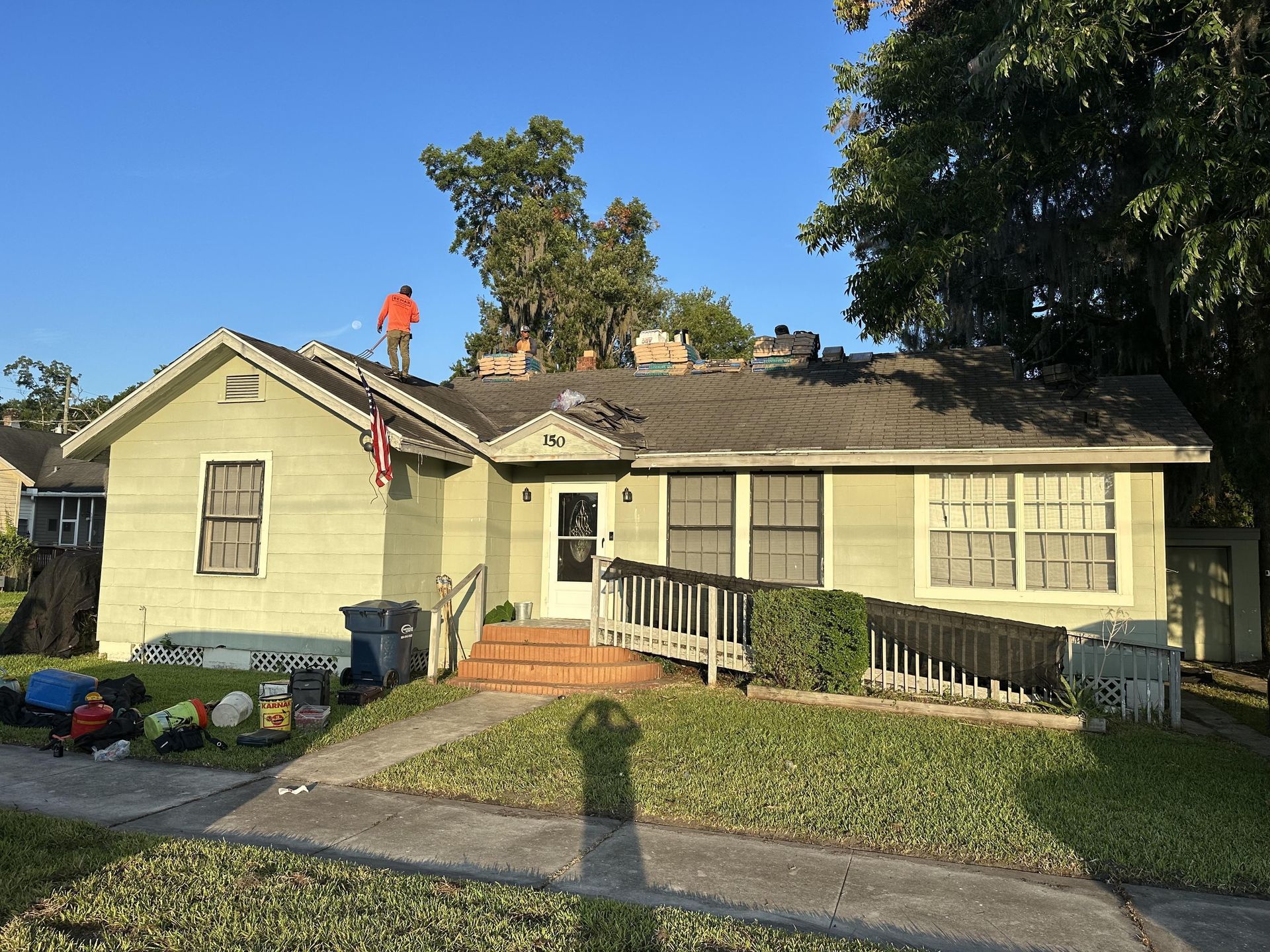 Single-story house with a ramp, front steps, and a large tree in the yard under a blue sky