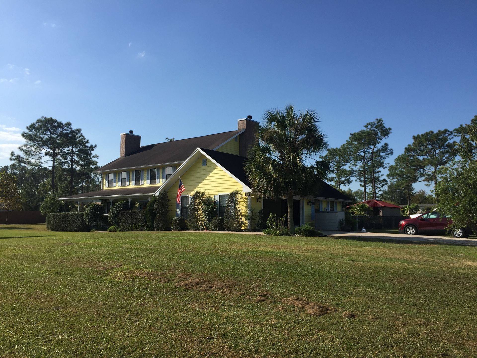 Large yellow house with a porch on a grassy lawn under a clear blue sky