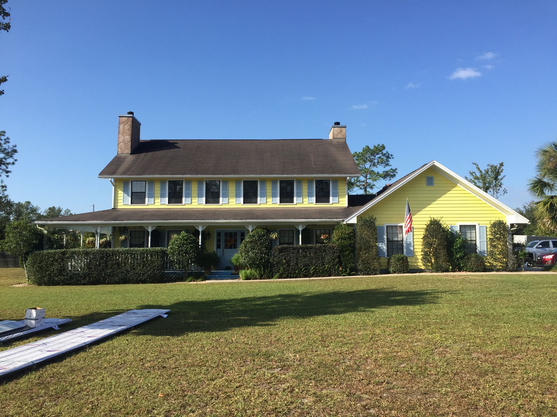 Yellow farmhouse with a porch and detached garage on a sunny grassy lot under a blue sky